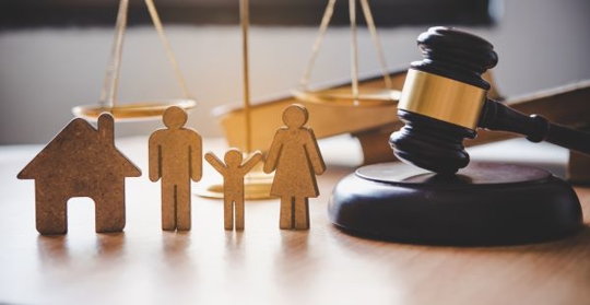 A gavel sits next to a wooden family and house cutout, likely representing a family law decision.