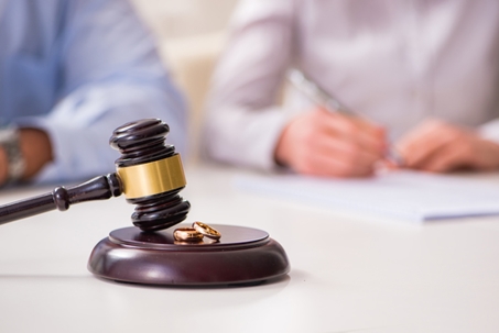 A gavel rests on a sound block with wedding rings alongside documents being signed.