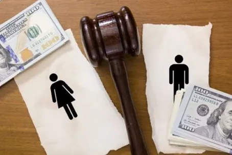 A judge's gavel resting between torn paper pieces depicting a female symbol with cash and a male symbol with cash.
