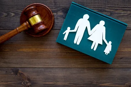 A judge's gavel beside a green book featuring paper cutouts of a family