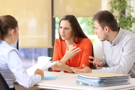 A couple arguing while meeting with an advisor or mediator across a desk.