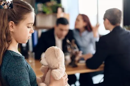 A young girl holding a teddy bear while adults argue in the background.