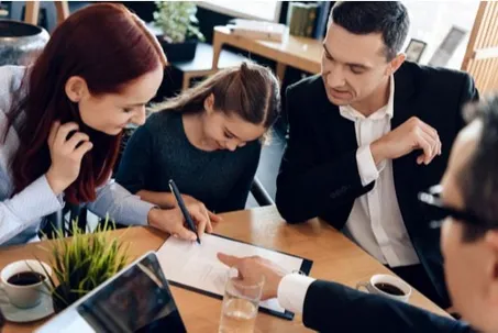 A family signing a document with an advisor or professional at a table.