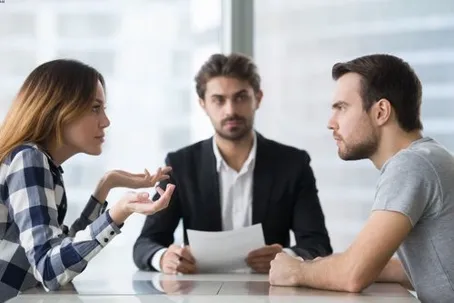 A man and a woman arguing during a mediation session with a professional seated between them.
