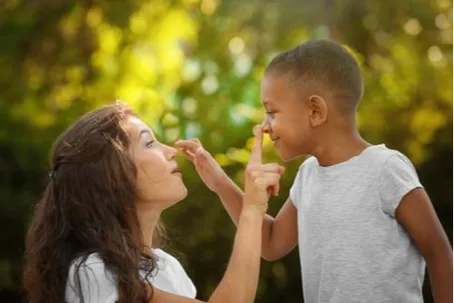 A woman and a young boy playfully touching noses outdoors.