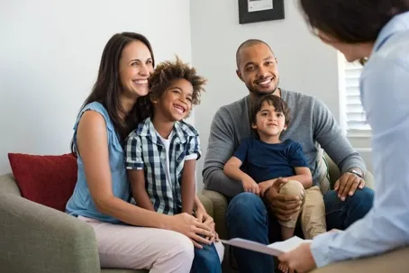 A smiling family of four sitting on armchairs talking with a professional.